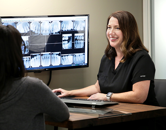Ashley Harrison sits at a desk and shows a patient her xrays on a screen.